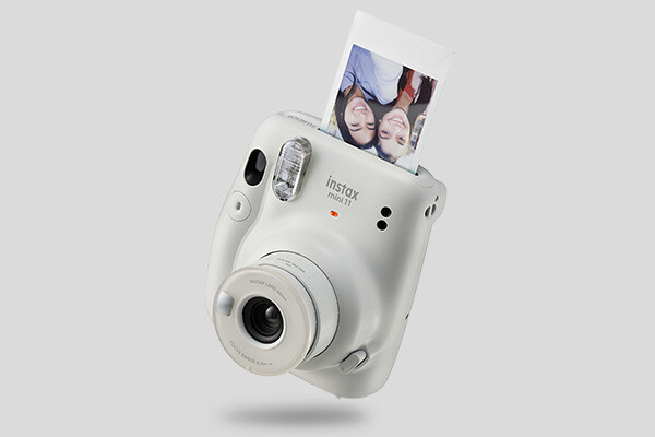 Witte instantcamera met net uitgeprinte foto van twee lachende mensen die samen een moment delen